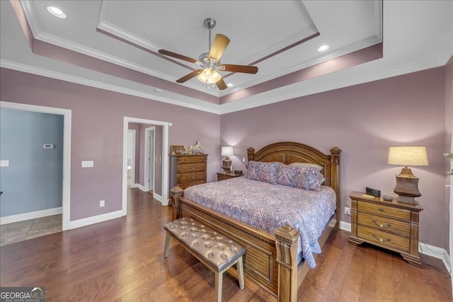 bedroom featuring ornamental molding, a tray ceiling, dark wood finished floors, and baseboards