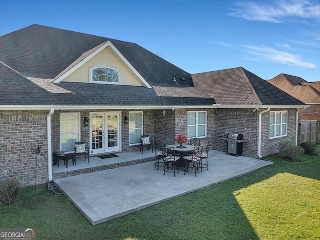 rear view of house featuring brick siding, a shingled roof, a patio area, and a yard