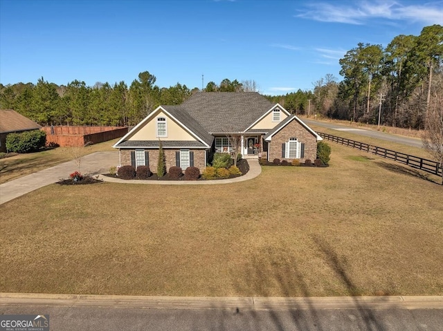 view of front of home featuring a wooded view, fence, concrete driveway, and a front yard