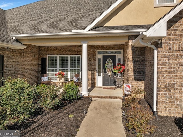 doorway to property featuring a shingled roof, a porch, and brick siding