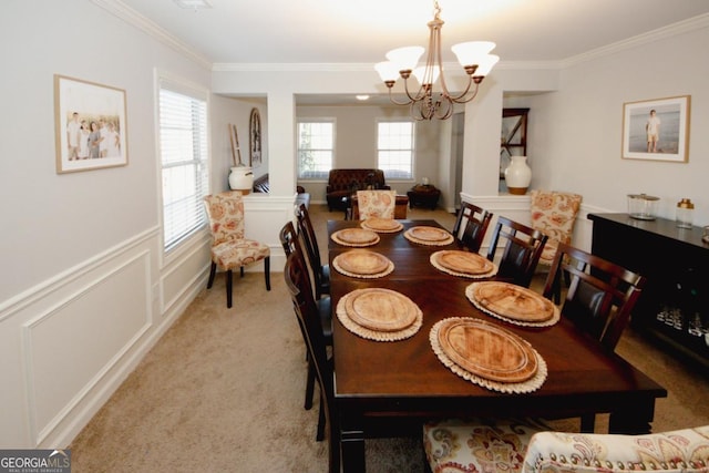 dining room featuring a chandelier, light colored carpet, a decorative wall, ornamental molding, and wainscoting