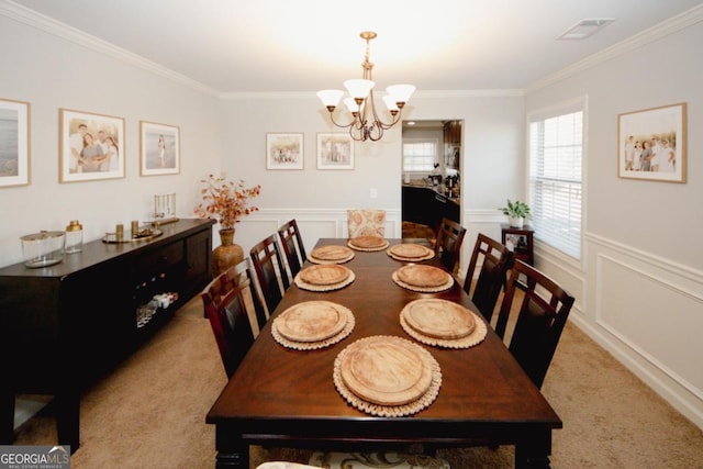 dining space with a notable chandelier, light carpet, visible vents, wainscoting, and crown molding