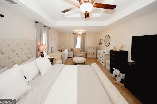 bedroom featuring light carpet, a tray ceiling, visible vents, and a ceiling fan