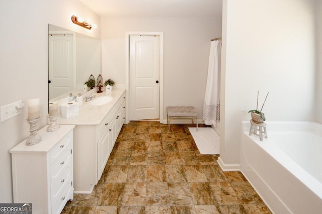 bathroom featuring stone finish floor, vanity, baseboards, and a bath