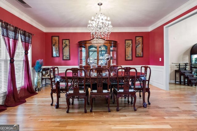dining area with a wainscoted wall, visible vents, light wood finished floors, and an inviting chandelier