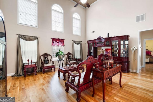 living area featuring baseboards, visible vents, a towering ceiling, ceiling fan, and wood finished floors