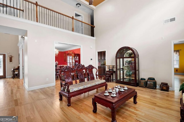 living room with a towering ceiling, visible vents, light wood-style flooring, and baseboards