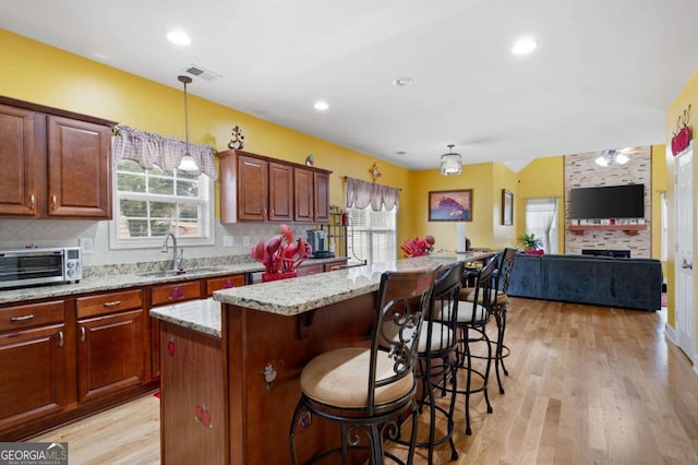 kitchen featuring tasteful backsplash, hanging light fixtures, open floor plan, a kitchen island, and a sink
