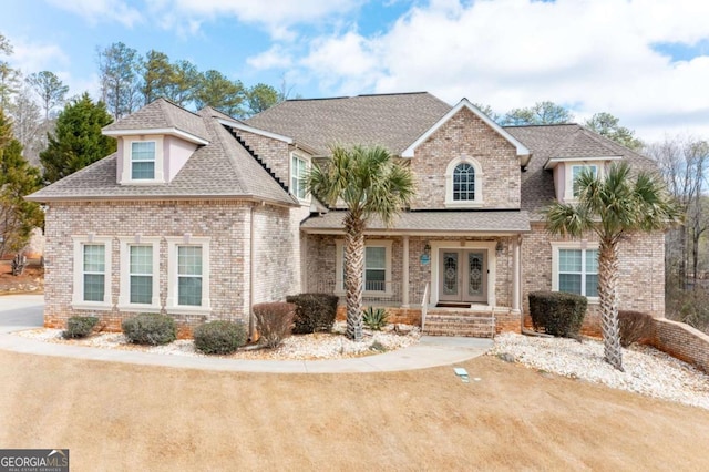 view of front of property with french doors, brick siding, and roof with shingles