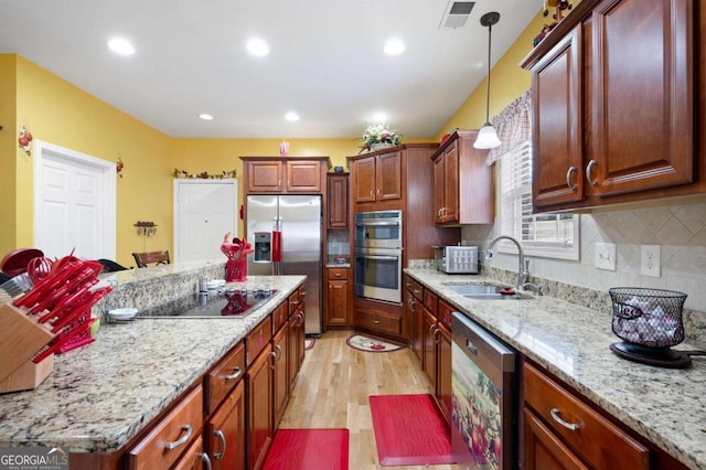 kitchen with light stone counters, stainless steel appliances, visible vents, hanging light fixtures, and a sink