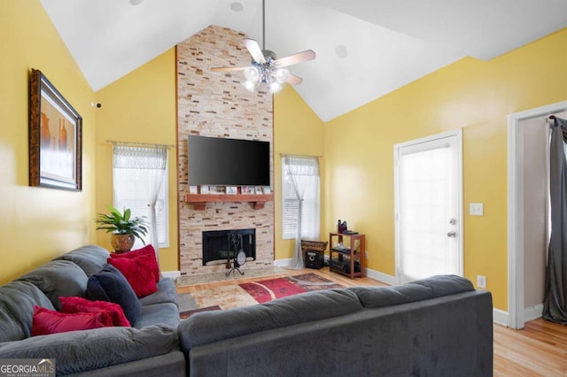 living room with light wood finished floors, a ceiling fan, a large fireplace, high vaulted ceiling, and baseboards