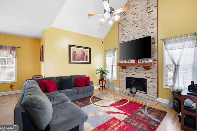 living room featuring high vaulted ceiling, a stone fireplace, baseboards, and wood finished floors