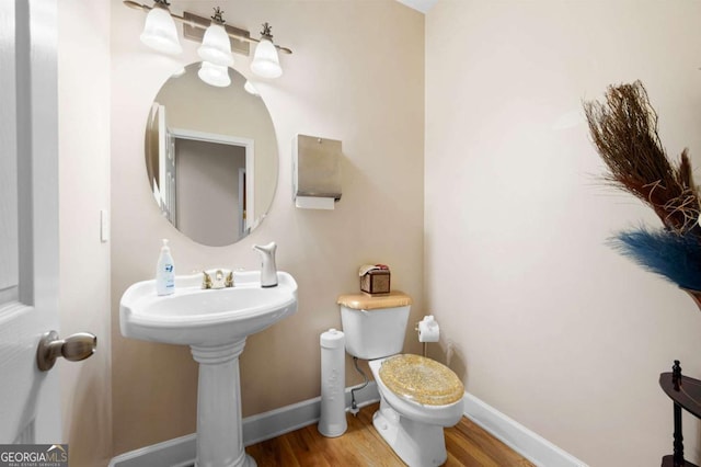 half bath with wood finished floors, toilet, and baseboards