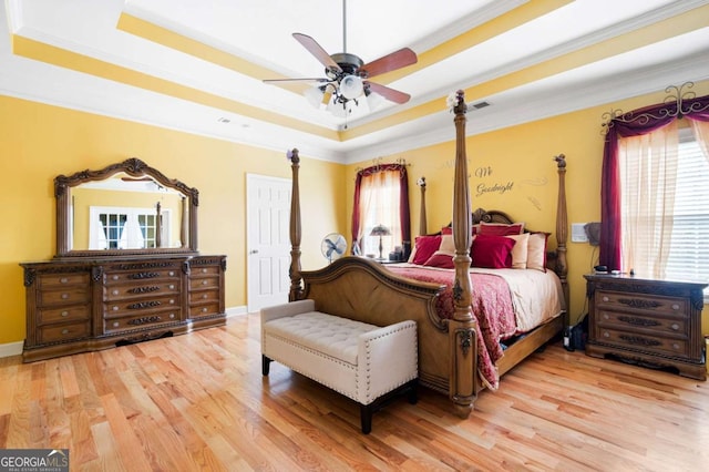 bedroom with light wood finished floors, a tray ceiling, and crown molding