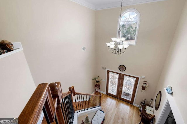 foyer entrance featuring a notable chandelier, baseboards, french doors, light wood finished floors, and crown molding