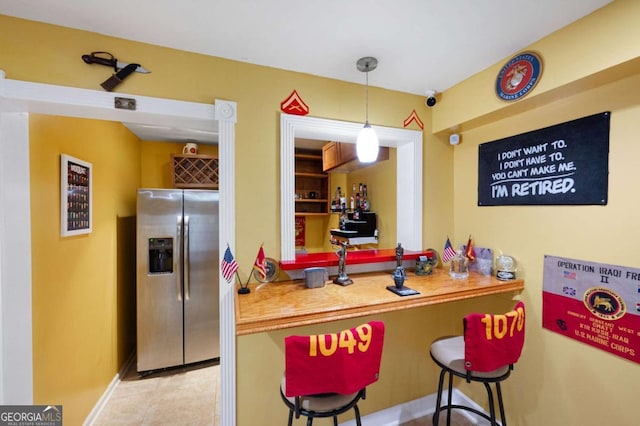 kitchen featuring decorative light fixtures, light tile patterned flooring, stainless steel fridge, a peninsula, and a kitchen bar