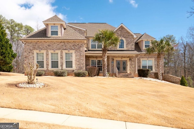 view of front of property featuring a shingled roof, brick siding, and a front lawn