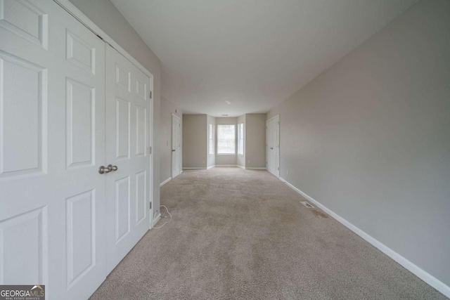 hallway with baseboards and light colored carpet