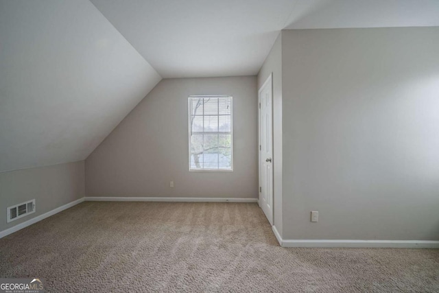 additional living space with light carpet, vaulted ceiling, visible vents, and baseboards