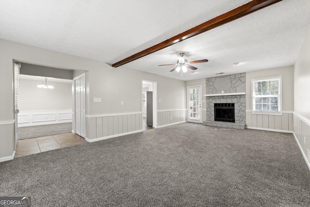 unfurnished living room featuring beam ceiling, a wainscoted wall, carpet flooring, a stone fireplace, and a textured ceiling