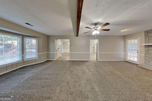 unfurnished living room with light colored carpet, visible vents, ceiling fan, and a textured ceiling