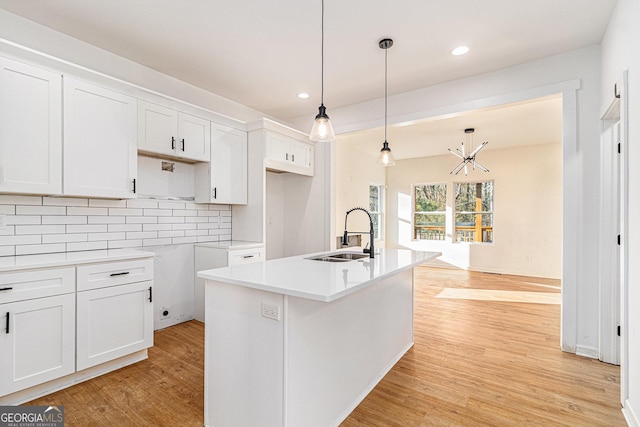 kitchen with a center island with sink, white cabinetry, light countertops, and a sink