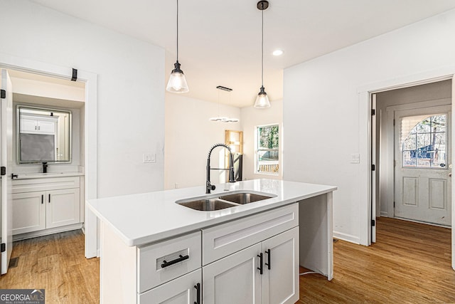 kitchen featuring light wood finished floors, an island with sink, hanging light fixtures, light countertops, and a sink