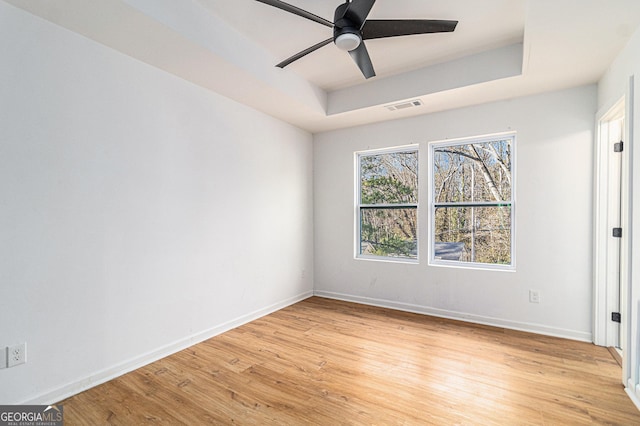 unfurnished room with a raised ceiling, visible vents, a ceiling fan, light wood-type flooring, and baseboards