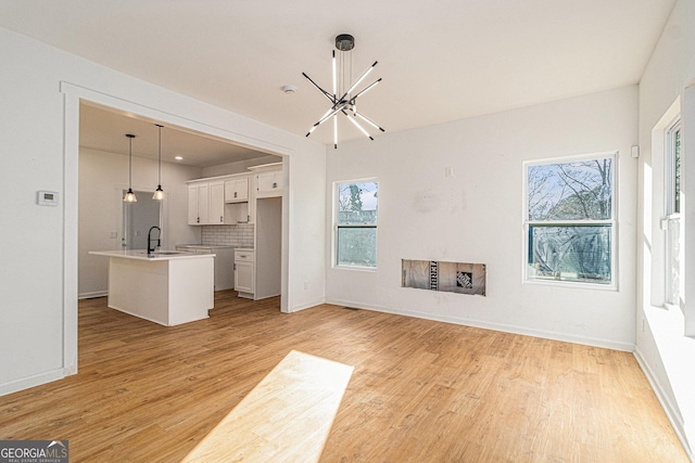 unfurnished living room with baseboards, light wood-style flooring, an inviting chandelier, a fireplace, and a sink