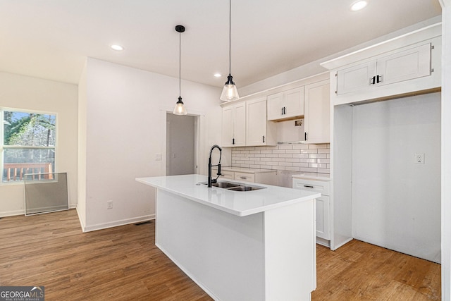 kitchen featuring a center island with sink, white cabinets, light countertops, pendant lighting, and a sink