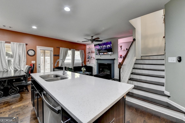 kitchen featuring dark wood-style flooring, light countertops, stainless steel dishwasher, a kitchen island with sink, and a sink