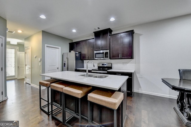 kitchen with a center island with sink, light countertops, appliances with stainless steel finishes, a sink, and a kitchen bar