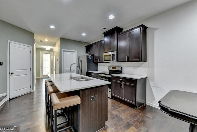 kitchen featuring stainless steel appliances, a sink, light countertops, a kitchen bar, and a center island with sink