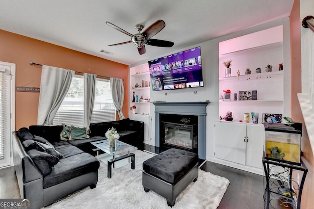 living room featuring a glass covered fireplace, visible vents, ceiling fan, and wood finished floors