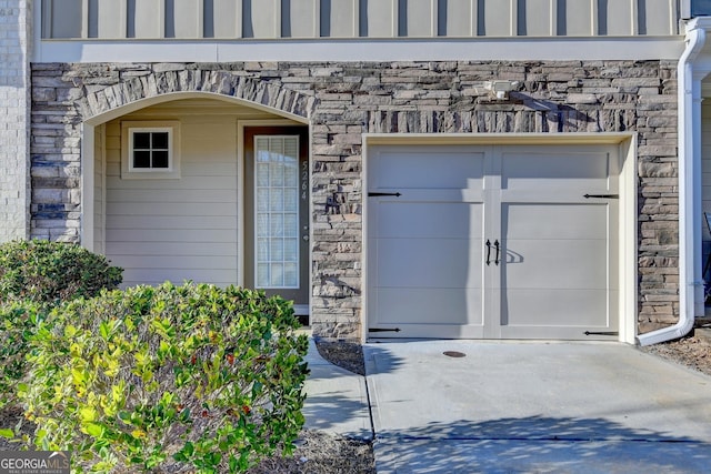 doorway to property with a garage, driveway, and stone siding