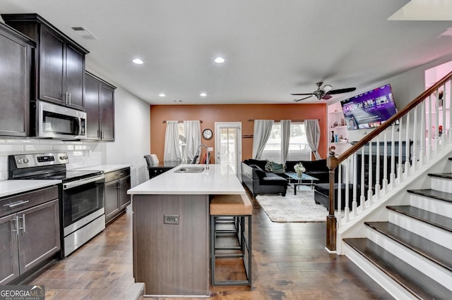 kitchen featuring a kitchen island with sink, stainless steel appliances, a kitchen breakfast bar, open floor plan, and light countertops