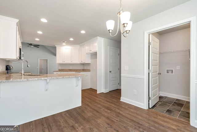 kitchen featuring hanging light fixtures, white cabinetry, a sink, a peninsula, and ceiling fan with notable chandelier