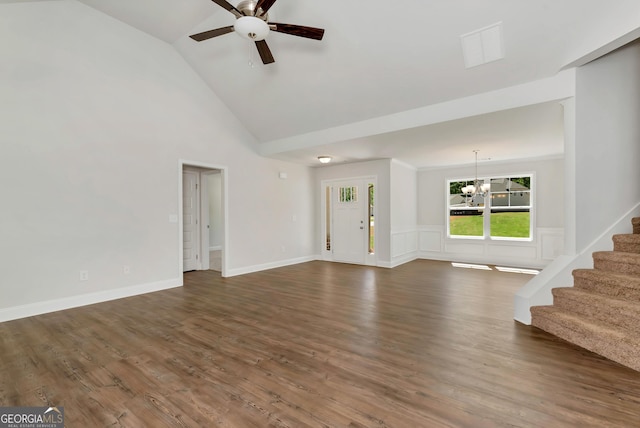 unfurnished living room featuring stairs, dark wood-type flooring, wainscoting, high vaulted ceiling, and ceiling fan with notable chandelier