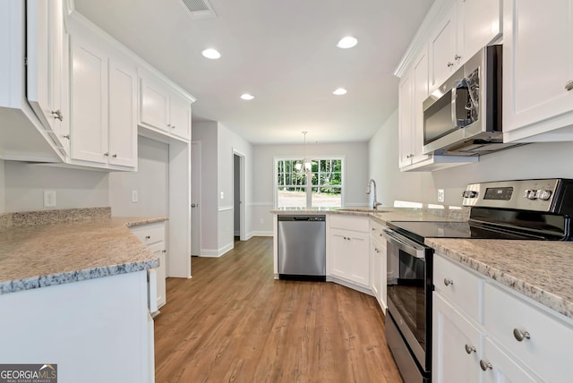 kitchen featuring stainless steel appliances, hanging light fixtures, light wood-style flooring, and white cabinets