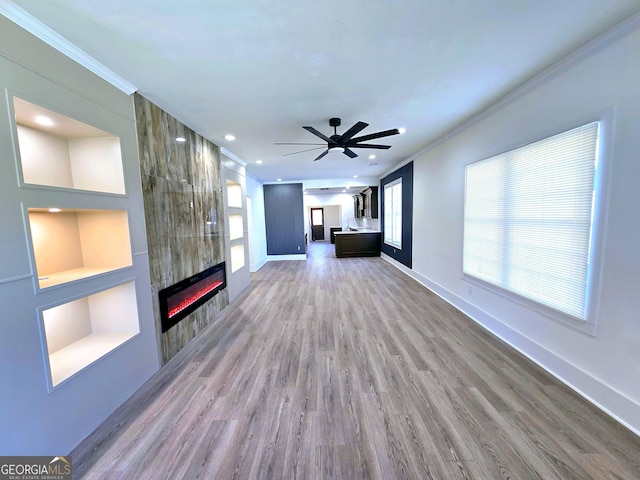 unfurnished living room featuring ornamental molding, a ceiling fan, wood finished floors, a tile fireplace, and baseboards