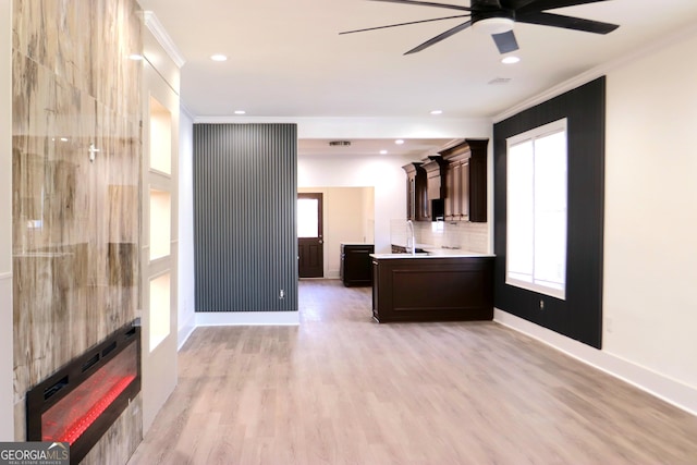 unfurnished living room with baseboards, light wood-type flooring, a sink, and crown molding