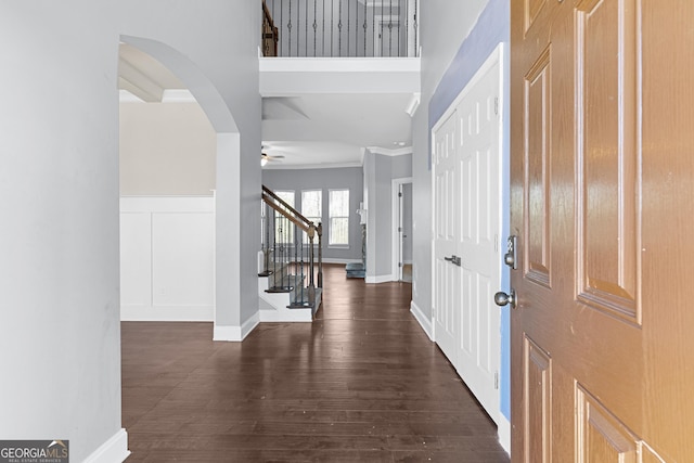 foyer entrance featuring stairway, ornamental molding, ceiling fan, dark wood-type flooring, and a decorative wall