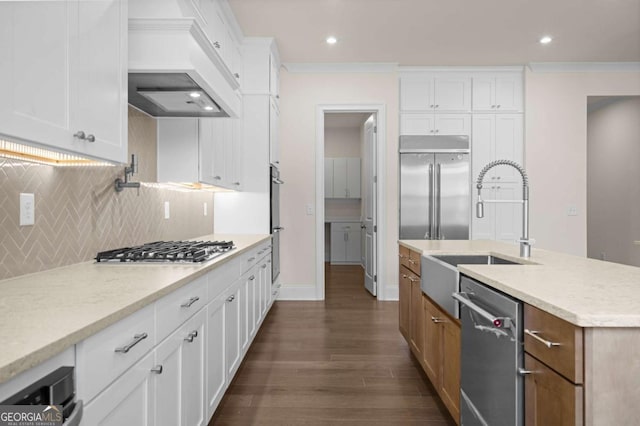 kitchen with appliances with stainless steel finishes, brown cabinetry, white cabinetry, and premium range hood