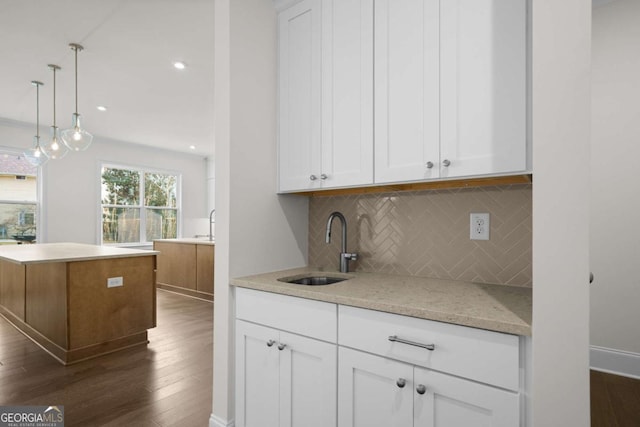 kitchen with white cabinets, dark wood-style floors, light stone counters, hanging light fixtures, and a sink