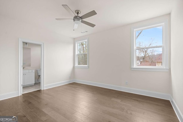 unfurnished bedroom featuring ensuite bathroom, ceiling fan, wood finished floors, visible vents, and baseboards