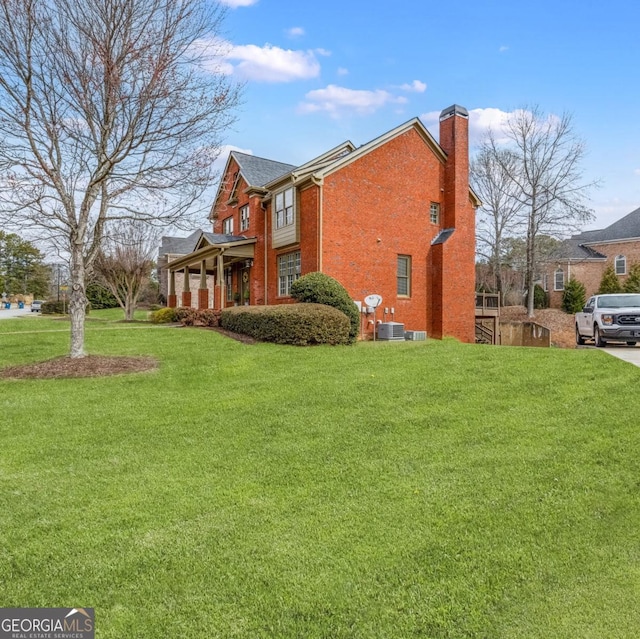 view of side of home with a yard, brick siding, a chimney, and central AC unit