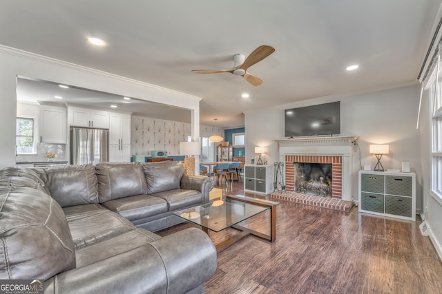 living area with ornamental molding, recessed lighting, a brick fireplace, and wood finished floors