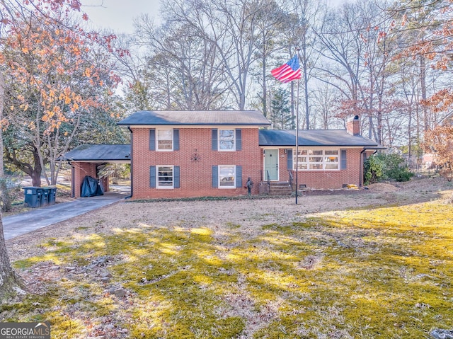 split level home with brick siding, driveway, a carport, a chimney, and a front yard