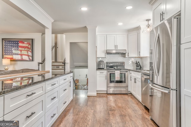 kitchen with crown molding, stainless steel appliances, white cabinets, dark stone countertops, and under cabinet range hood