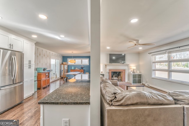 living room featuring a ceiling fan, ornamental molding, light wood-type flooring, a fireplace, and recessed lighting